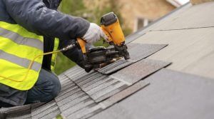 roofer using nail gun to install shingles